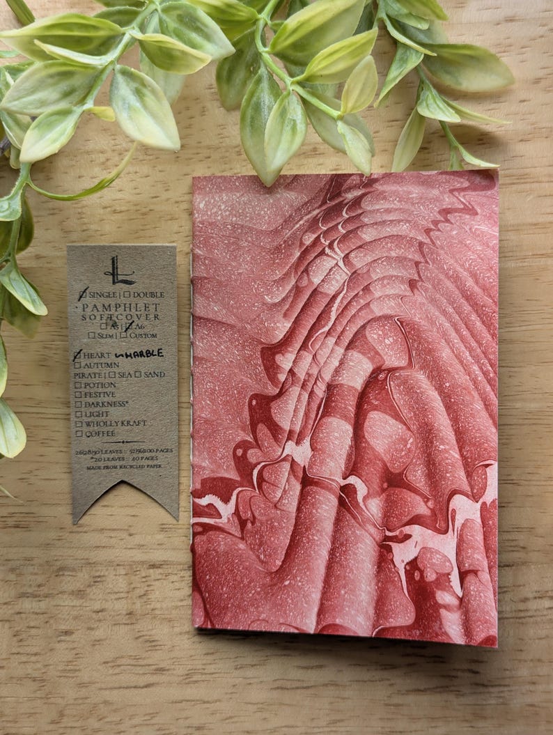 May include: A pamphlet cover with a red and white marbled design. The cover is next to a tag with text that reads "SINGLE DOUBLE PAMPHLET SOFA COVER HEART MARBLE". The tag is made from recycled paper.