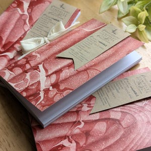May include: Notebooks with red and white marbled covers. Each notebook has a kraft paper tag attached with a white ribbon. The tags list options such as "Autumn", "Darkness", and "Coffee".