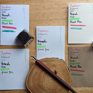 May include: An overhead shot of stationery supplies on a wooden surface. The image features ink, a pen, and several cards with handwritten text and color swatches. The text includes "Fineliner", "Ballpoint", "Gel", "Brush", "Nib", and "Paint Pen".
