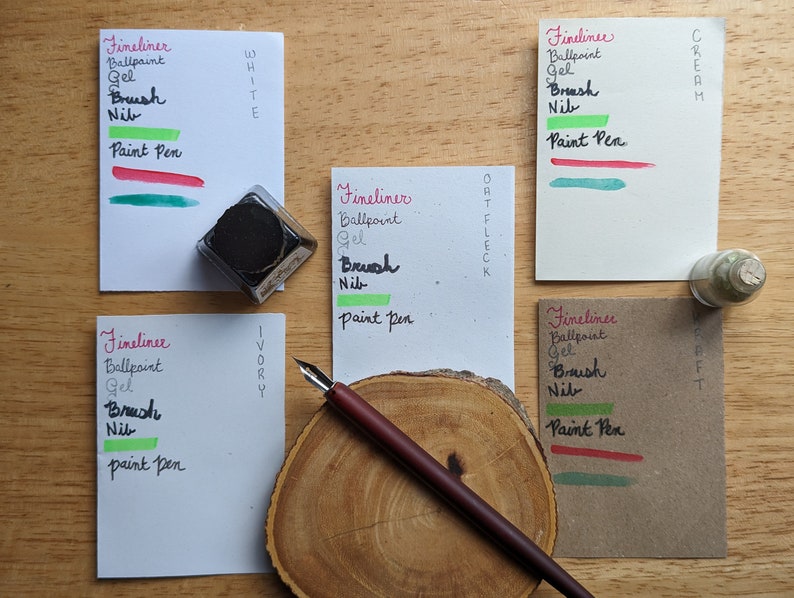 May include: An overhead shot of stationery supplies on a wooden surface. The image features ink, a pen, and several cards with handwritten text and color swatches. The text includes "Fineliner", "Ballpoint", "Gel", "Brush", "Nib", and "Paint Pen".
