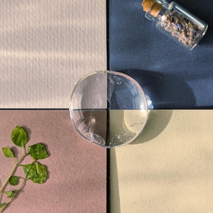 May include: A four-quadrant display featuring textured squares labelled COTTON in off-white, LAVENDER in dark blue with a small glass vial of dried lavender, ALMOND in mauve with a green sprig, and KIWI in light yellow, centred by a clear glass disc.