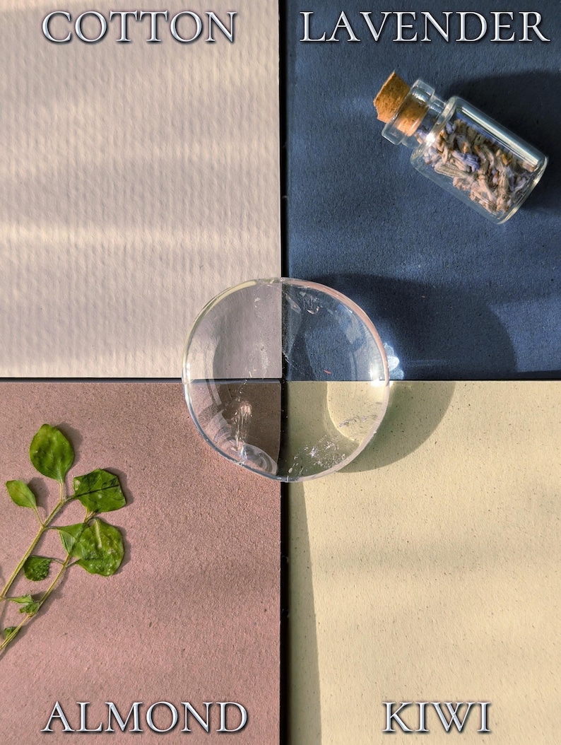 May include: A four-quadrant display featuring textured squares labelled COTTON in off-white, LAVENDER in dark blue with a small glass vial of dried lavender, ALMOND in mauve with a green sprig, and KIWI in light yellow, centred by a clear glass disc.