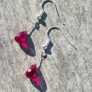 May include: A pair of silver dangle earrings with teardrop-shaped red gemstone accents.