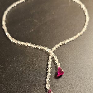 Könnte beinhalten: Eine silberne Halskette mit einer Kristallkette und zwei baumelnden rosafarbenen tropfenförmigen Steinen.
