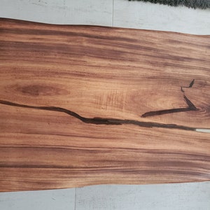 May include: A large, rectangular wooden table top with a natural, brown wood grain. The table top has a crack running through it that has been filled with clear epoxy resin.