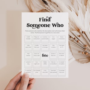 May include: A white game card with the text "Find Someone Who" in a decorative font. The card includes a grid of prompts like "Is left handed" and "Likes spicy food", designed for a party game. The word "free" is also on the card.