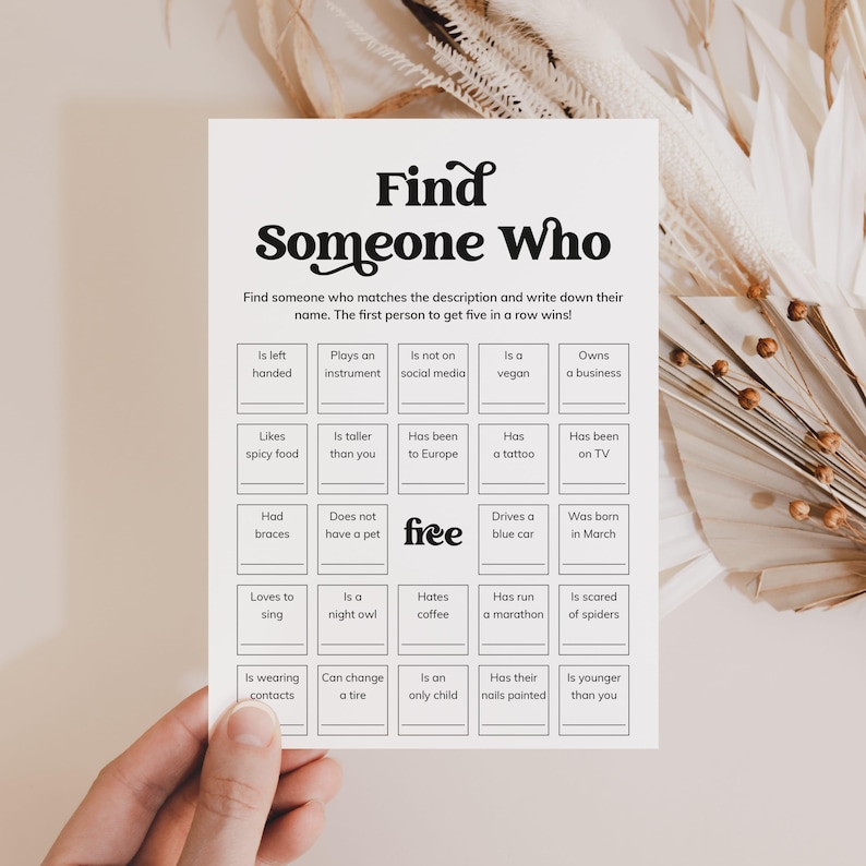 May include: A white game card with the text "Find Someone Who" in a decorative font. The card includes a grid of prompts like "Is left handed" and "Likes spicy food", designed for a party game. The word "free" is also on the card.