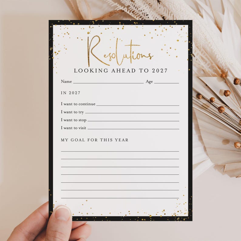 May include: A rectangular paper card titled Resolutions Looking Ahead To 2027 with gold glitter accents on a white background and a black border. The card includes lines for name, age, and prompts for goals including continue, try, stop, and visit.