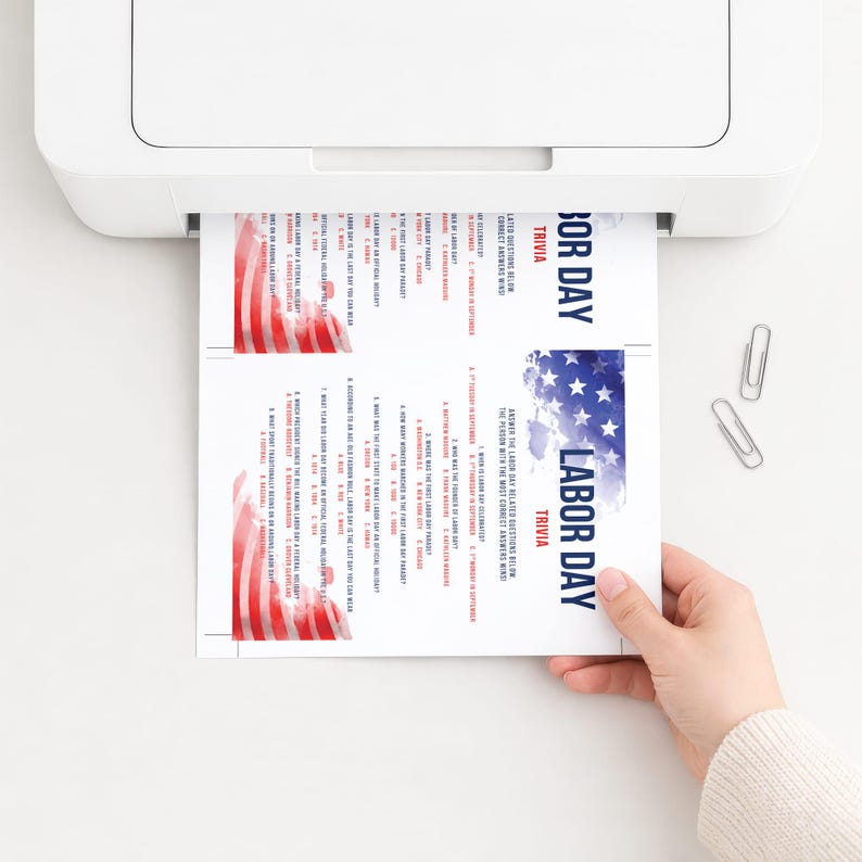 May include: A white sheet of paper printed with two identical Labor Day trivia games, featuring red and white stripes and blue stars with white text reading Labor Day Trivia and a list of questions about the holiday, emerging from a white printer.