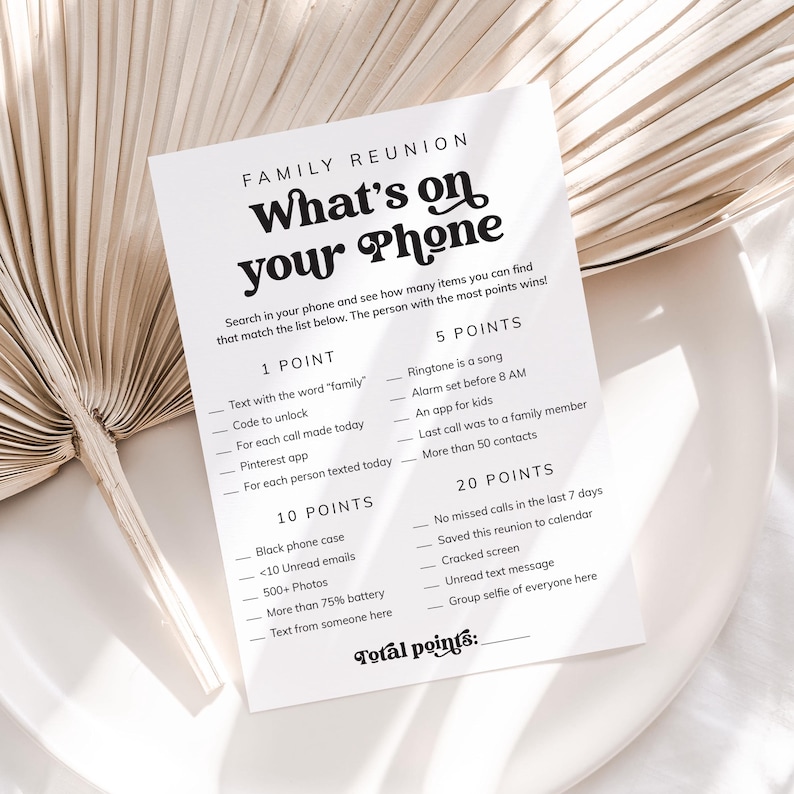 May include: A printable game card for a family reunion. The card has a black and white design with the title "What's on your Phone" and a list of items to find on a phone for points. The items include things like "Text with the word 'family'" and "Group selfie of everyone here".