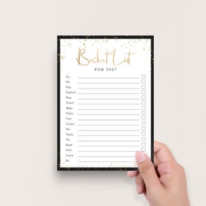 K&ouml;nnte beinhalten: Eine rechteckige Bucket-List-Karte f&uuml;r 2027 mit schwarzem Rand und goldenen Glitzerakzenten. Die wei&szlig;e Mitte zeigt den goldenen Text Bucket List, den schwarzen Text FOR 2027 sowie eine Liste mit horizontalen Linien und leeren K&auml;stchen.