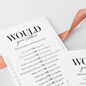 K&ouml;nnte beinhalten: Eine wei&szlig;e Karte mit schwarzem Text, der "WOULD you rather" lautet und eine Reihe von "Would You Rather"-Fragen auflistet. Die Karte liegt auf einer rosa Oberfl&auml;che.