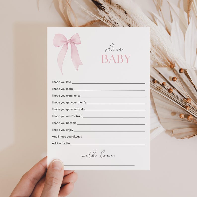 May include: A white card with a pink bow and the text "dear BABY" in black. The card has a list of phrases with blank lines for writing, such as "I hope you love", "I hope you learn", and "I hope you experience". The card ends with the text "with love."