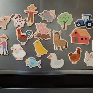 Magnete hängen auf dem Kühlschrank. Zu sehen sind folgende Bauernhof Motive: Baum, Windmühle, Pferd, Traktor, Küken, Fisch, Schaf, Scheune, Maus, Huhn, Hahn, Hase, Ente, Obstkorb, Katze, Kuh, Hund, Vogelscheuche, Schwein, Bauer.