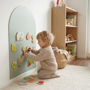 May include: A sage green arched wall-mounted magnetic board featuring various wooden garden-themed shapes including a greenhouse, vegetables, and a person with a watering can, with additional loose pieces resting on the floor.