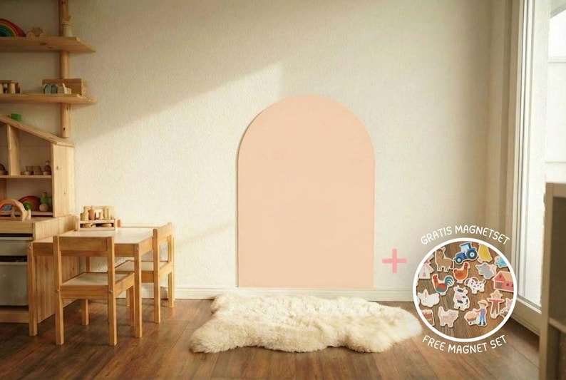 Ein heller Raum mit Holzmöbeln, darunter ein Tisch und Stühle sowie eine Spielküche. Ein großer, pfirsichfarbener Bogen ist an die Wand gemalt. Ein weißer Schaffellteppich liegt auf dem Holzboden.