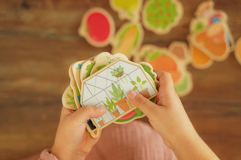 Obst und Gemüse Magnete werden von einem Kind in der Hand gehalten. Ein Gewächshaus ist ganz oben zu sehen.