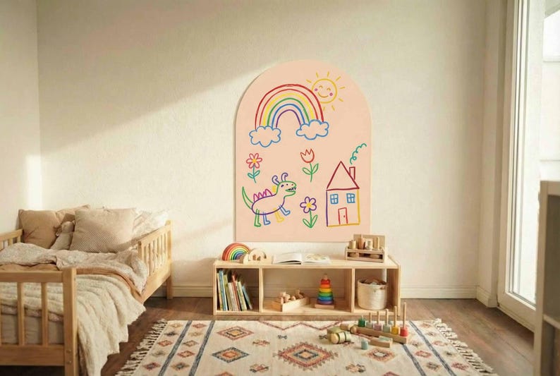 May include: An arched wall decal featuring a light peach background with colorful child-like drawings including a rainbow, a smiling sun, a green dinosaur, a house with a chimney, and various flowers, applied to a plain interior wall surface.