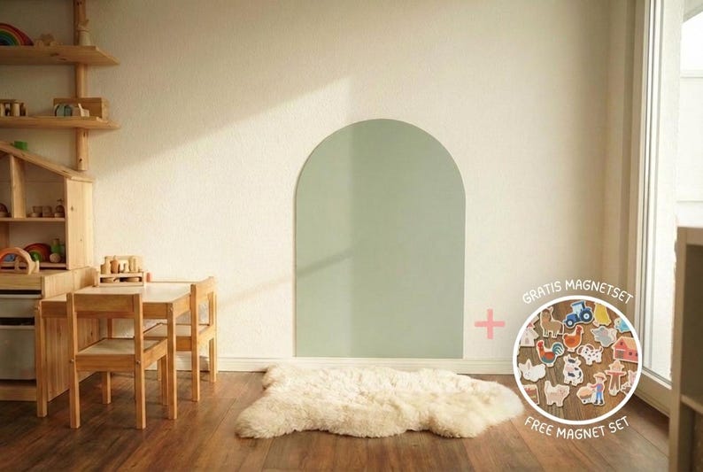 May include: A sage green arch-shaped wall board with a smooth surface, accompanied by a circular set of assorted farm-themed magnets featuring animals, a tractor, and a barn, labeled with the text GRATIS MAGNETSET FREE MAGNET SET.