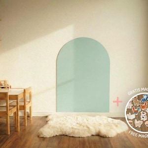 Ein heller Raum mit Holzmöbeln, darunter ein Tisch und Stühle, und ein Regal mit Spielzeug. Ein großer, hellgrüner Bogen ist an die Wand gemalt. Ein weißer Schaffellteppich liegt auf dem Holzboden.
