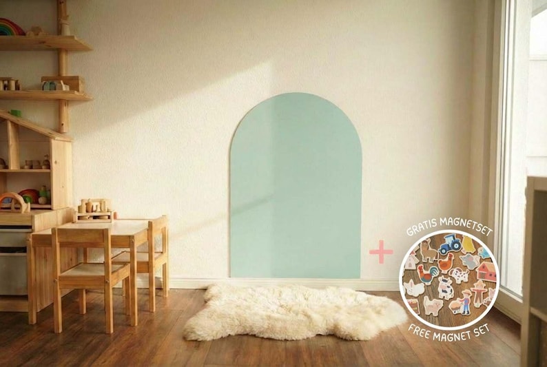 Ein heller Raum mit Holzmöbeln, darunter ein Tisch und Stühle, und ein Regal mit Spielzeug. Ein großer, hellgrüner Bogen ist an die Wand gemalt. Ein weißer Schaffellteppich liegt auf dem Holzboden.