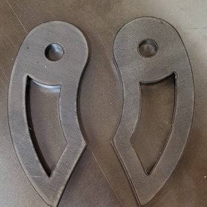 May include: Two black metal pieces with a curved shape and a hole in the center. The pieces are cut out with a design that resembles a crescent moon.