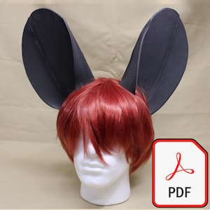 May include: A red wig with large, black, pointed ears is displayed on a white mannequin head. The image includes a PDF icon in the lower right corner. The wig's hair is styled with a layered cut.