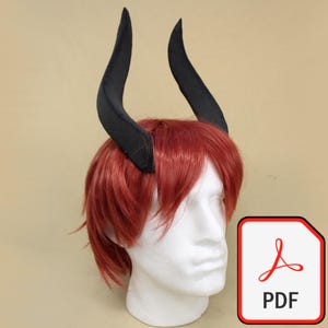Puede incluir: Cuernos de diablo negros unidos a una peluca roja, exhibidos en una cabeza de maniquí blanca. Los cuernos son curvos y puntiagudos. La peluca tiene un estilo en capas. Un icono PDF está en la esquina inferior derecha.
