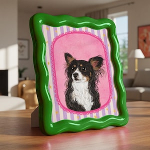Op de afbeelding: Een groene, golvende fotolijst met een hondenportret. De hond heeft zwart, wit en bruin haar en grote oren. De lijst heeft een roze en gestreepte achtergrond met een decoratieve rand.