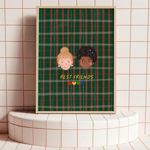 Puede incluir: Una impresi&oacute;n art&iacute;stica enmarcada con dos caras ilustradas de amigas sobre un fondo de cuadros verdes y rojos. Las palabras "BEST FRIENDS" est&aacute;n escritas debajo, con corazones coloridos. La obra de arte se exhibe sobre una superficie de baldosas blancas.