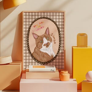 Op de afbeelding: Een ingelijst kattenportret met een bruin-witte kat genaamd Simba. Het kunstwerk staat tegen een geruite achtergrond en bevat de tekst "You are so loved."