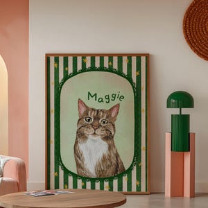 Op de afbeelding: Een ingelijst portret van een kat genaamd Maggie. De kat is bruin en wit met groene ogen, tegen een lichtgroene achtergrond. De lijst heeft een groen en wit gestreept patroon met gouden accenten.
