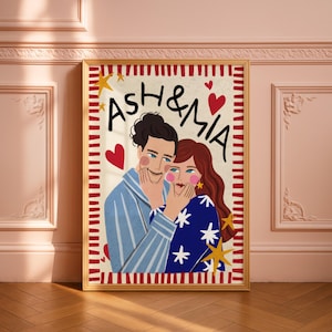 K&ouml;nnte beinhalten: Ein gerahmter rechteckiger Wandkunstdruck mit einer stilisierten Illustration von zwei Personen und dem Text ASH & MIA. Die linke Person tr&auml;gt ein blau gestreiftes Hemd, die rechte Person ein blaues Hemd mit wei&szlig;en Sternen.