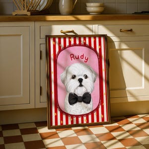 Op de afbeelding: Een ingelijst portret van een witte hond genaamd Rudy, met een zwarte vlinderdas. Het portret staat tegen een roze achtergrond met een rood-witte gestreepte rand. De lijst is bruin.