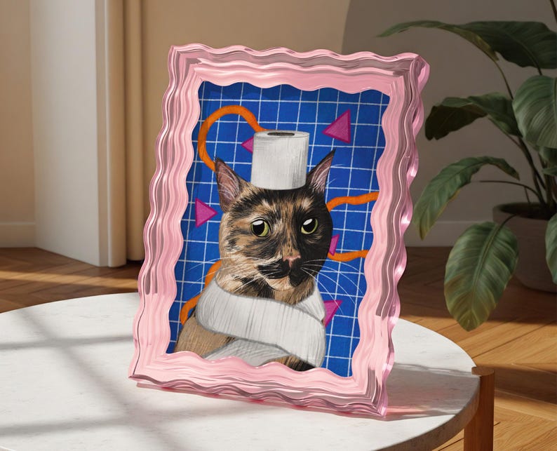 May include: A pink framed artwork depicting a cat with a toilet roll on its head and wrapped around its neck. The background is blue with a grid pattern, orange lines, and pink triangles. The frame has a wavy edge.