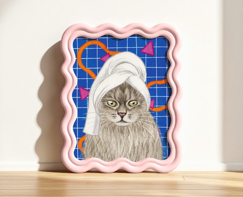 May include: A framed print of a cat wearing a white towel. The cat has grey fur and green eyes. The background is blue with a grid pattern and orange and pink geometric shapes. The frame is pink.