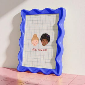 Puede incluir: Un marco de fotos azul con bordes ondulados que contiene un papel cuadriculado con dos caras ilustradas y el texto "BEST FRIENDS" en rojo. Las caras representan a dos mujeres, una rubia con un mo&ntilde;o y la otra con pelo rizado oscuro y gafas.