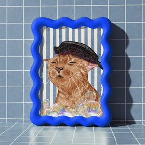 May include: A framed illustration of a ginger cat being brushed in a bath, with bubbles. The frame is a wavy, bright blue. The background features blue and white vertical stripes.