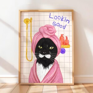 May include: Framed art print showing a black cat in a pink towel turban and robe, with the words "Lookin Good" in blue. The cat is in a bathroom setting with a gold shower head and bottles on a shelf.