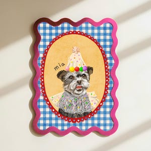 Op de afbeelding: Een ingelijste illustratie van een hond met een feesthoed en een trui. De hond staat in een ovale lijst met een rode geschulpte rand, tegen een blauw-wit geruite achtergrond. De naam "mia" staat boven de hond.