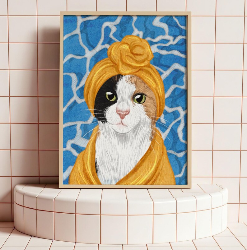 May include: A framed art print of a calico cat in a yellow turban and robe. The cat has green eyes and a pink nose. The background features a blue and white abstract design. The artwork is displayed on a white tiled pedestal.