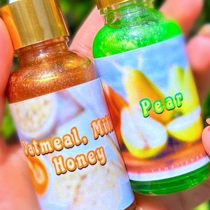 Puede incluir: Dos peque&ntilde;as botellas de vidrio con tapas doradas. Una botella contiene un l&iacute;quido dorado brillante, con la etiqueta "Oatmeal, Milk, Honey". La otra botella tiene un l&iacute;quido verde y una etiqueta con una pera y la palabra "Pear".