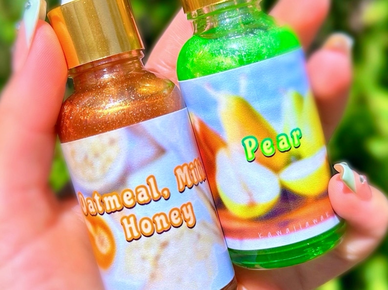 Puede incluir: Dos peque&ntilde;as botellas de vidrio con tapas doradas. Una botella contiene un l&iacute;quido dorado brillante, con la etiqueta "Oatmeal, Milk, Honey". La otra botella tiene un l&iacute;quido verde y una etiqueta con una pera y la palabra "Pear".