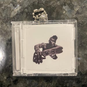 May include: A clear plastic CD case with a black and white photo of a person on the front. The case has a silver chain attached to it.