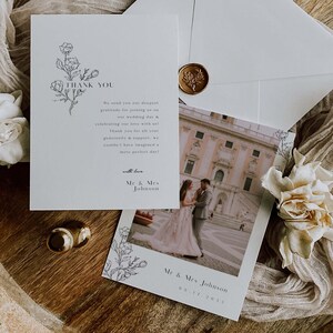 Könnte beinhalten: Eine weiße Dankeskarte mit einem floralen Design und dem Text "Danke" in Schwarz. Die Karte enthält ein Foto eines Paares vor einem Gebäude mit dem Text "Mr. & Mrs. Johnson 08.11.2023".