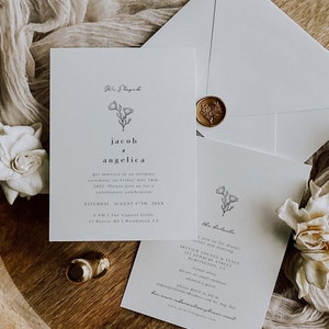 May include: A white wedding invitation with a floral design and the text "We Eloped, Jacob & Angelica, got married in an intimate ceremony on Friday July 14th, 2021. Please join us for a celebratory celebration, Saturday, August 17th, 20XX, 6 PM | The Capitol Grille, 23 Beaver Rd | Woodstock VT". The invitation is on a wooden surface with a white fabric and a gold wax seal.