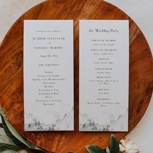 May include: Wedding ceremony program cards with a watercolor mountain landscape design. The cards list the wedding party, the officiant, and the order of the ceremony.