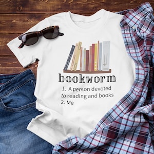 May include: White t-shirt with a graphic of a bookshelf full of books and the text "bookworm" with the definition: "1. A person devoted to reading and books 2. Me"