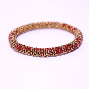 Puede incluir: Un brazalete de cuentas doradas y rojas. El brazalete está hecho de pequeñas cuentas redondas que están tejidas juntas en un patrón. Las cuentas son una mezcla de doradas y rojas, y el brazalete tiene aproximadamente 1,2 cm de ancho.