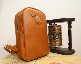 VAJRAMAMLA Leather backpack with hand-carved brass emblem | Unisex Brown Rucksack | Handmade in Nepal